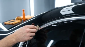 Close-up of gloss black vinyl covering chrome window trim during a chrome delete install