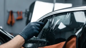 Gloved hand squeegeeing window tint film onto car glass during a window tint installation