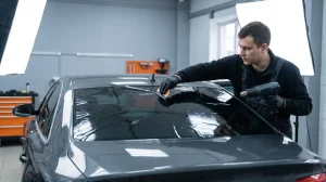 Technician installing window tint film on a sedan rear window with a heat gun